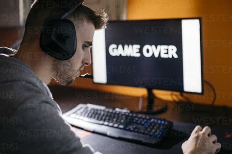 Young man sitting at his PC, looking at screen with game over text ...